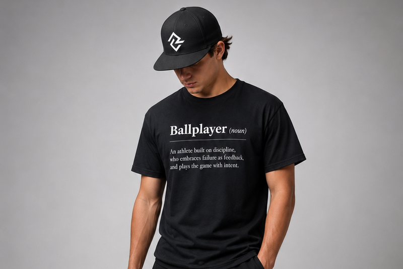 Model wearing the black BALLPLAYER premium baseball t-shirt and black Rake City RC logo snapback.