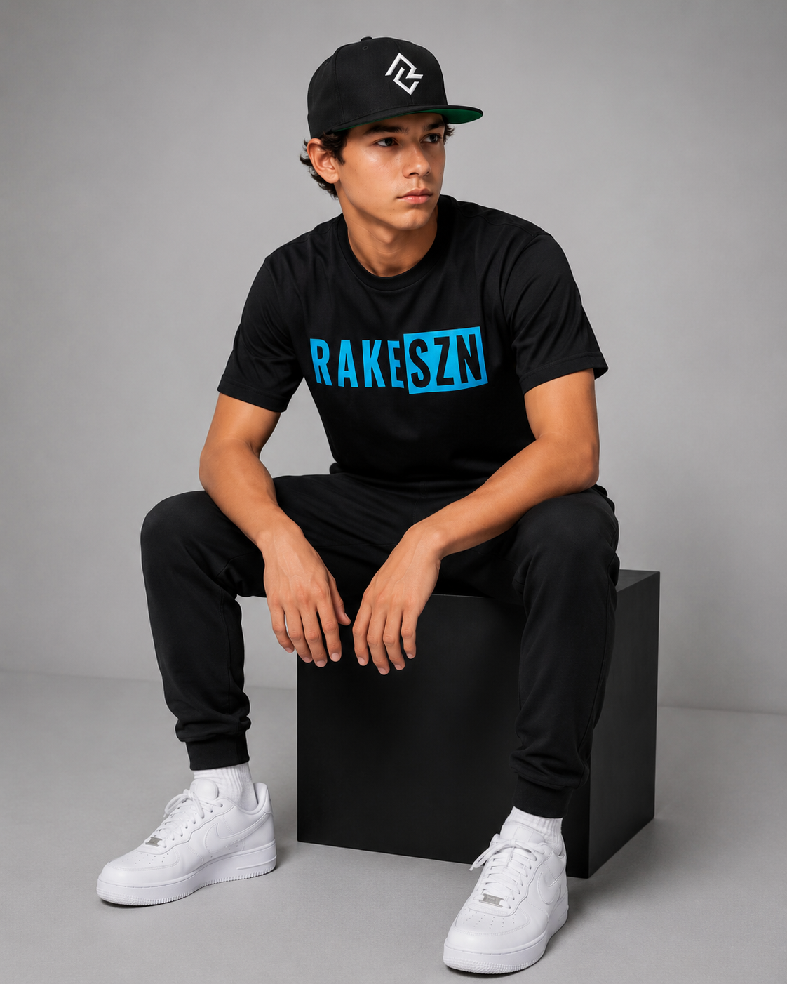Model wearing the black RAKE SZN t-shirt and black RC snapback by Rake City.