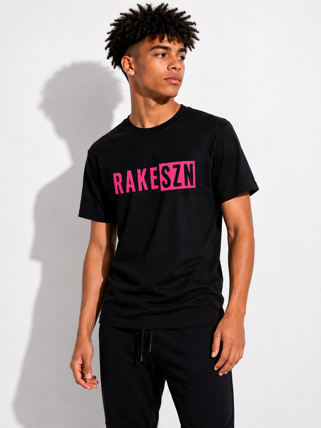 Model wearing the black RAKE SZN t-shirt  with pink by Rake City.